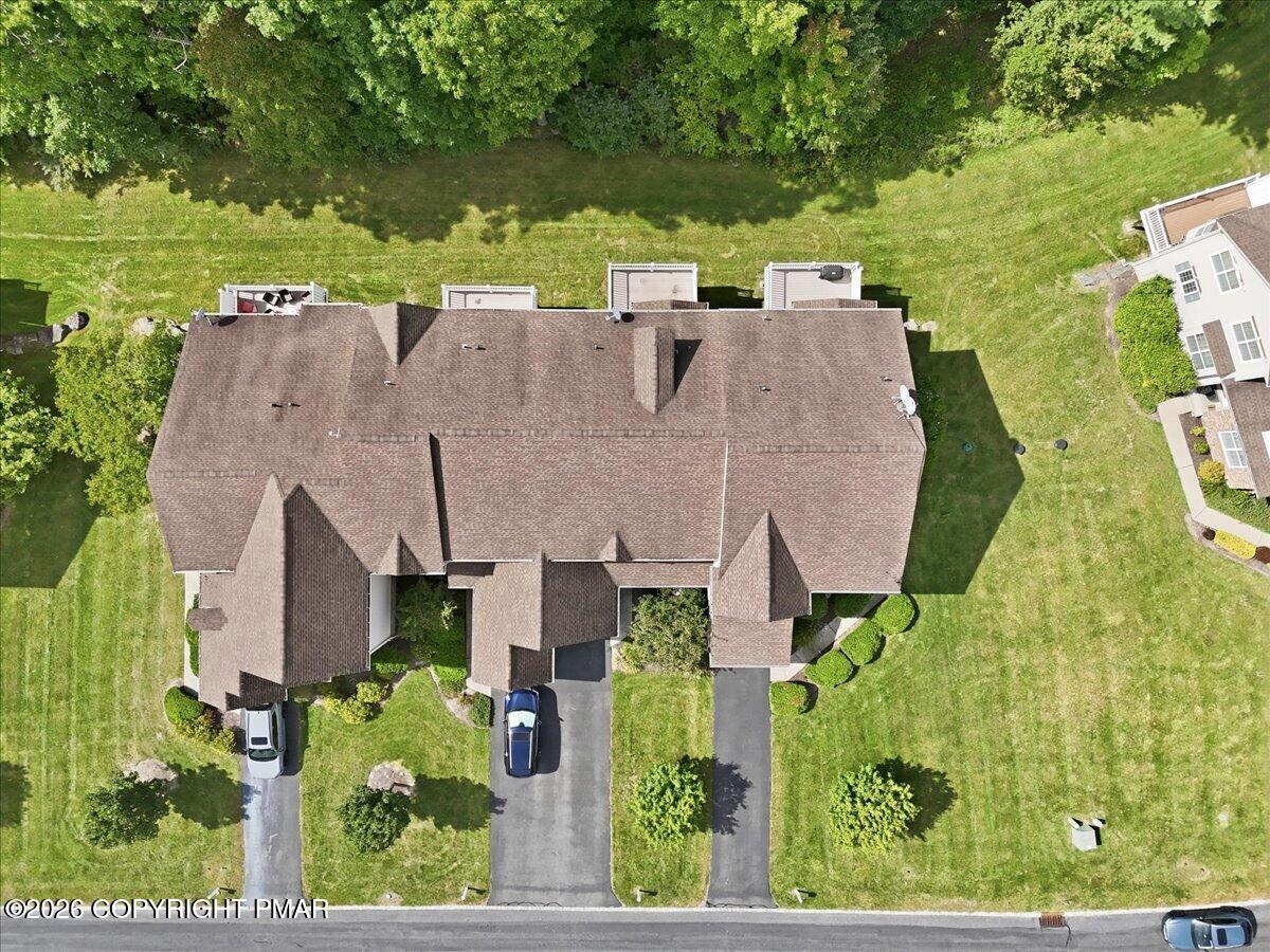 Aerial view of a residential building with a brown roof, multiple driveways, and surrounding lawn.
