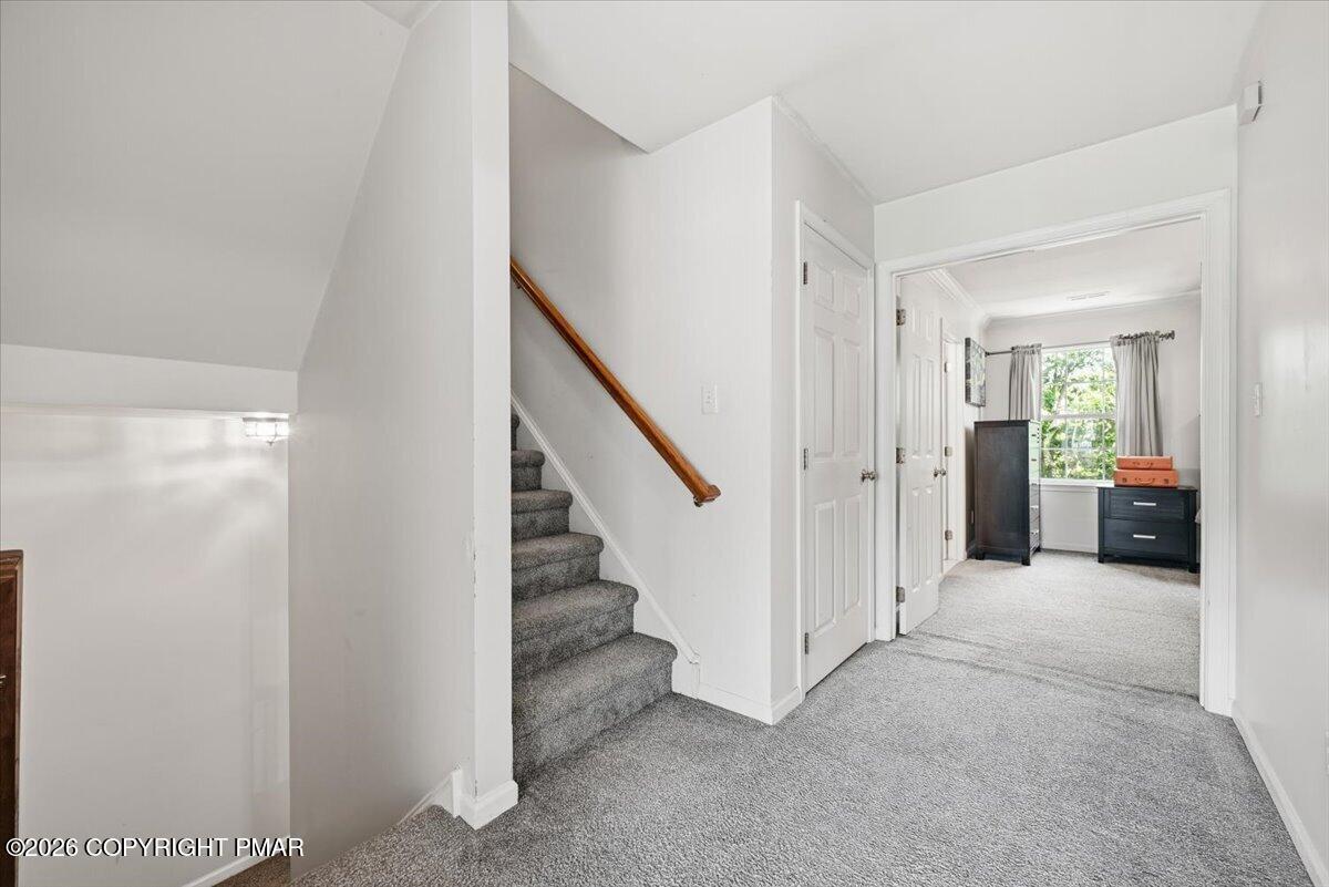 Carpeted upstairs hallway with stairs and a wooden handrail leading to a bedroom.