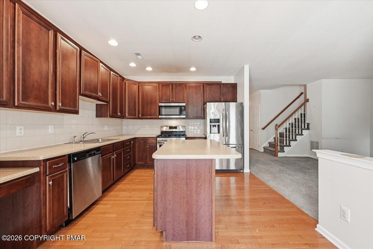 Kitchen with dark wood cabinetry, a central island, stainless steel appliances, and hardwood floors.