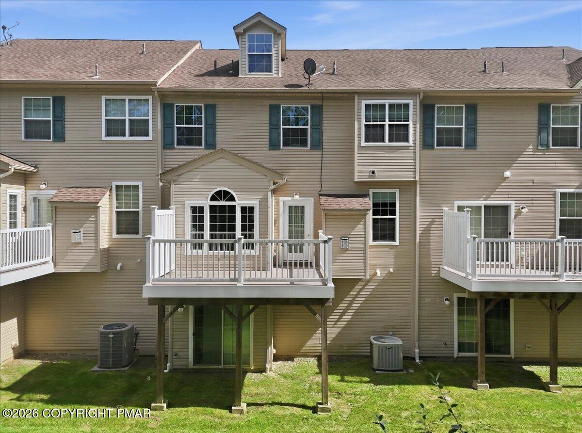 Rear exterior of a tan-sided townhouse with raised white-railed decks and a small lawn.