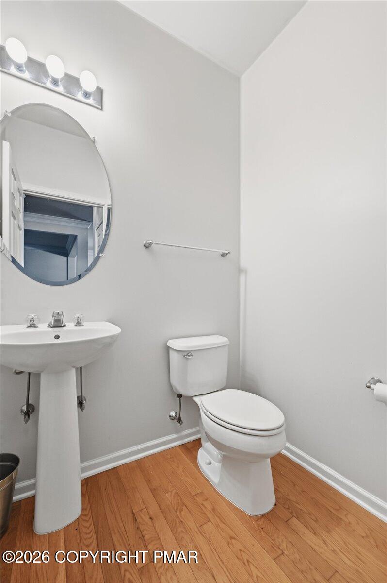 Bathroom with a pedestal sink, toilet, oval mirror, and hardwood flooring.