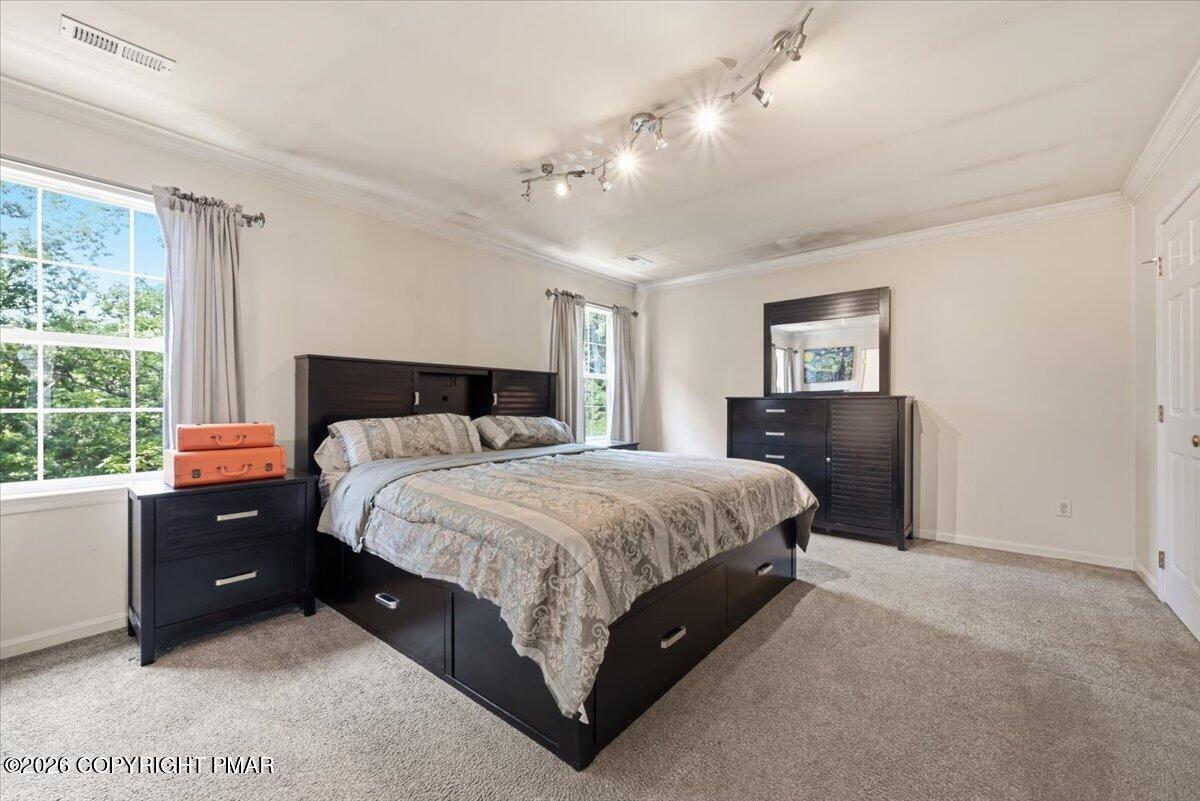 Furnished bedroom with a large bed, dark wood furniture, and two curtained windows.
