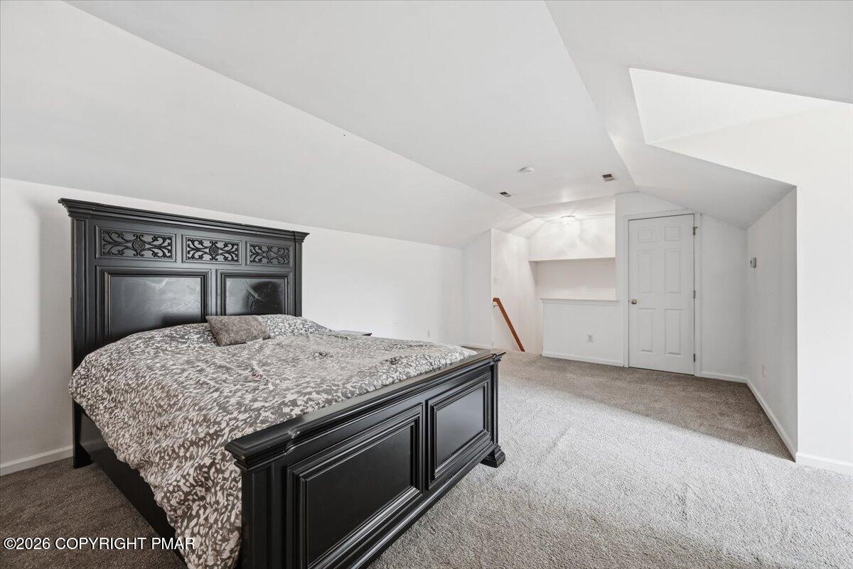 Furnished bedroom with an ornate black bed beneath a sloped ceiling and gray carpeting.