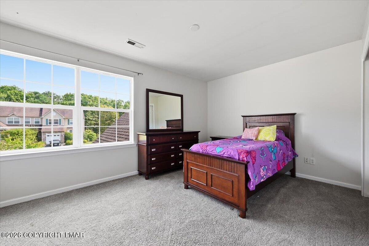 Furnished bedroom with a dark wood bed, vivid purple bedding, and a large window overlooking greenery.