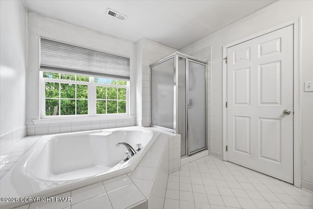 Bright tiled bathroom with a corner soaking tub, glass shower, and large window.