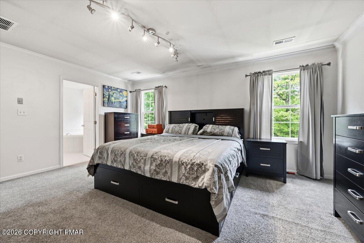 Bedroom with a dark storage bed, gray patterned bedding, and large curtained windows.
