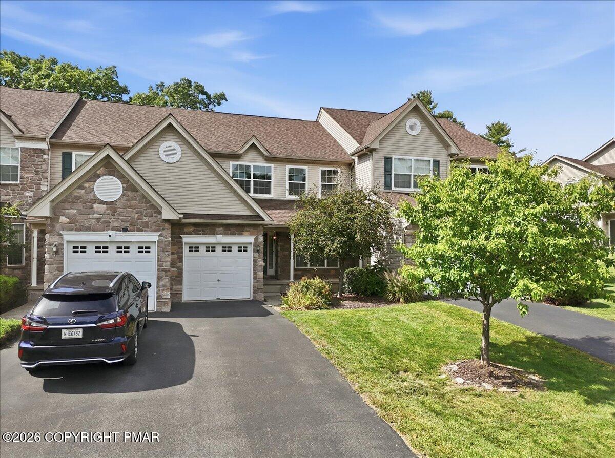 Attached home with stone facade, two garage doors, and a tree-lined front lawn.