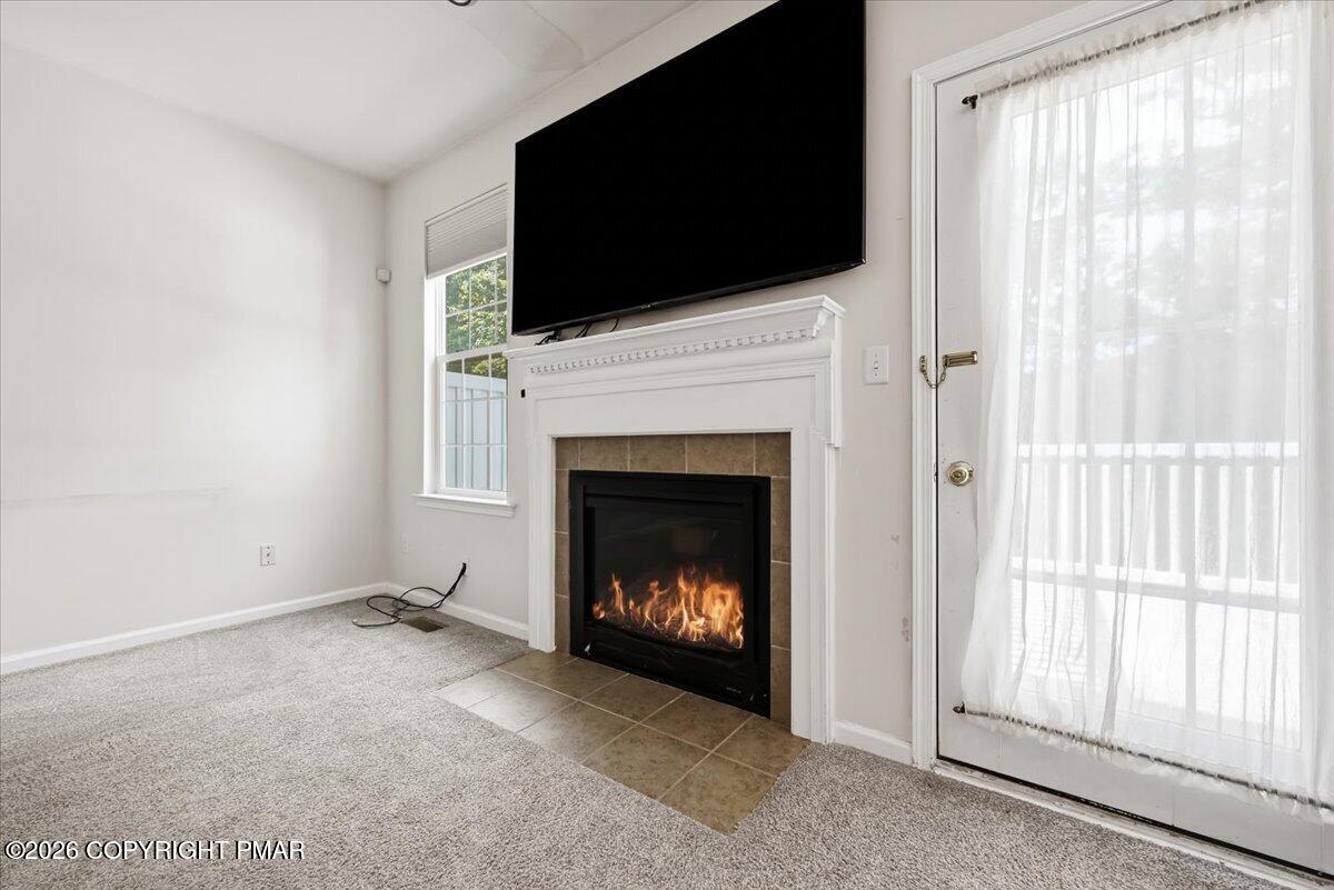 Living room with a lit fireplace, large wall-mounted television, and curtained glass door.