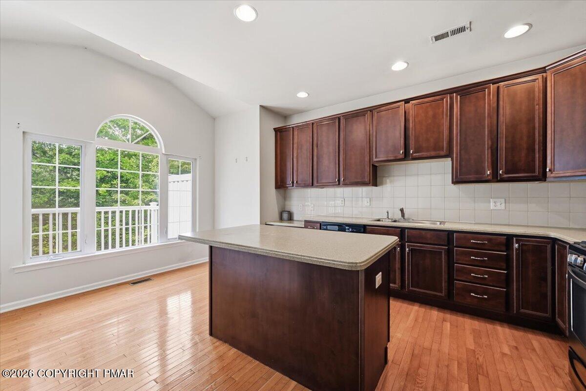 Kitchen with dark wood cabinets, a central island, hardwood floors, and a large arched window.