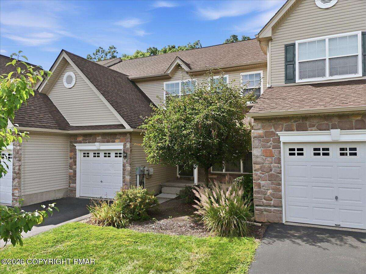 Beige multi-level home with two white garage doors, stone accents, and a landscaped front yard.