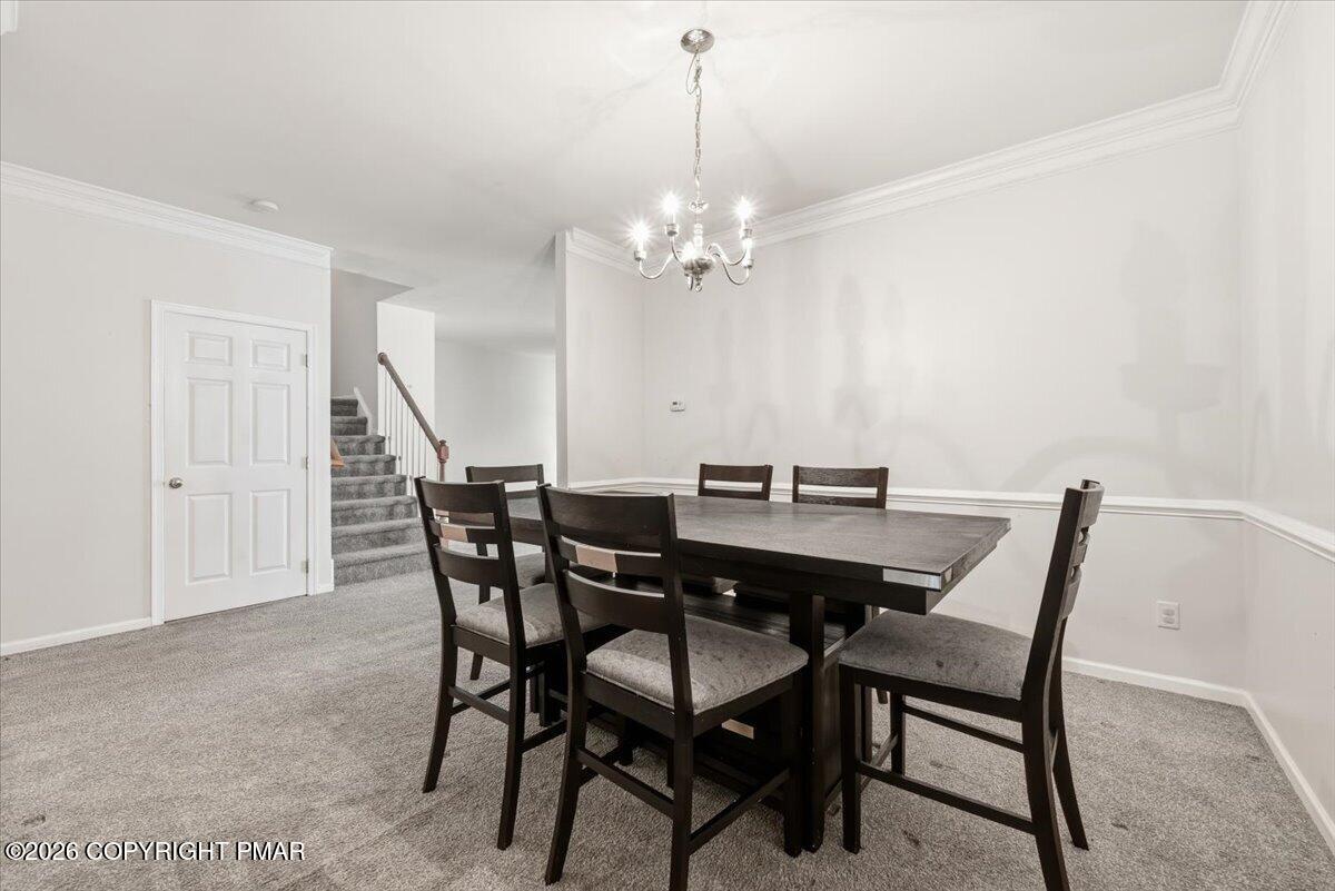 Dining room with a dark table and chairs, gray carpet, chandelier, and staircase.