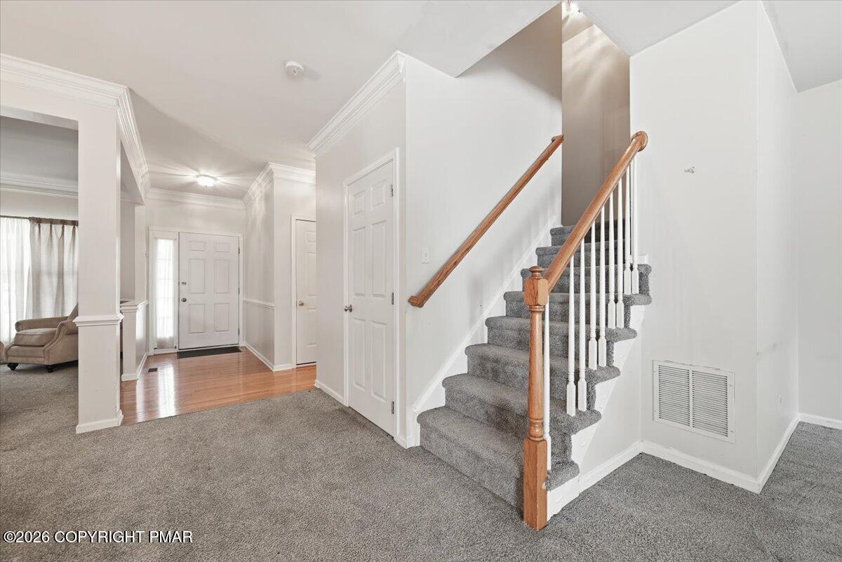 Entry hall with a gray-carpeted staircase, wood handrail, and hardwood near the front door.