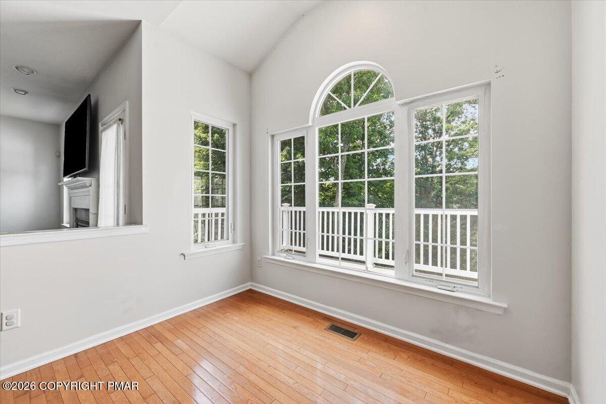 Bright room with hardwood floors and a large arched window overlooking trees.