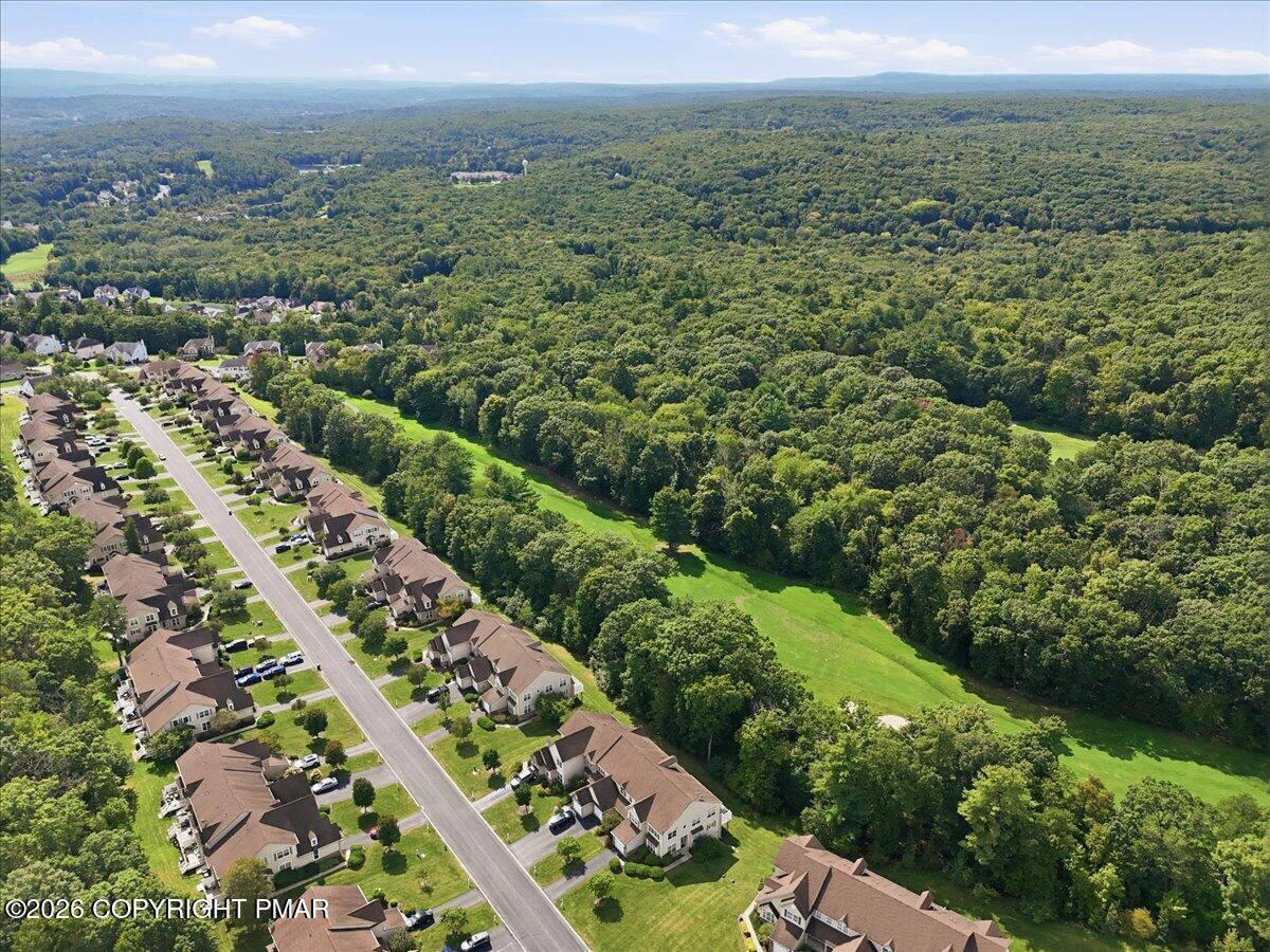 Aerial view of homes beside a broad wooded landscape and distant rolling hills.