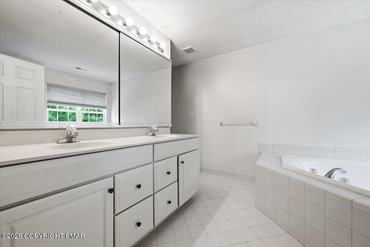 Bathroom with a long white double vanity, large mirror, and built-in tiled tub.