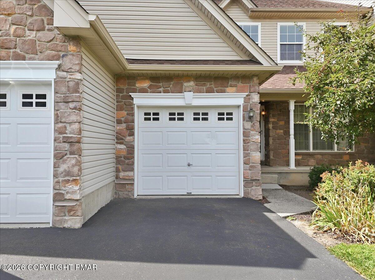 House exterior with white garage doors, a stone facade, and a covered front entry.