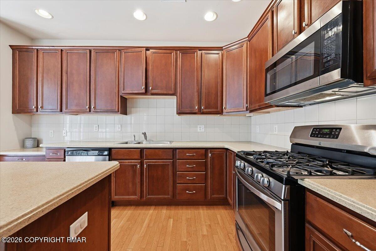 Kitchen with dark wood cabinets, stainless steel gas range and microwave, and hardwood flooring.