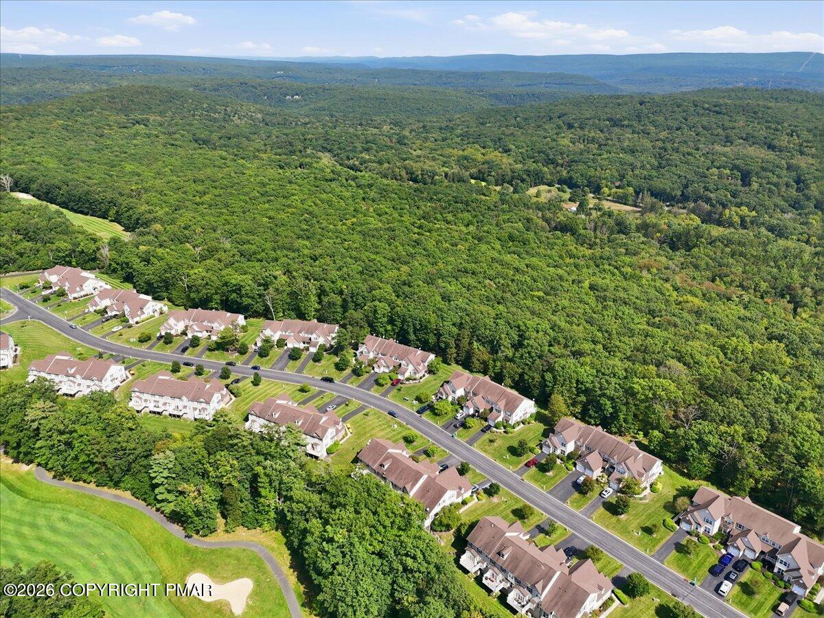 Aerial view of homes beside dense forest and a golf course, with wooded ridges in the distance.