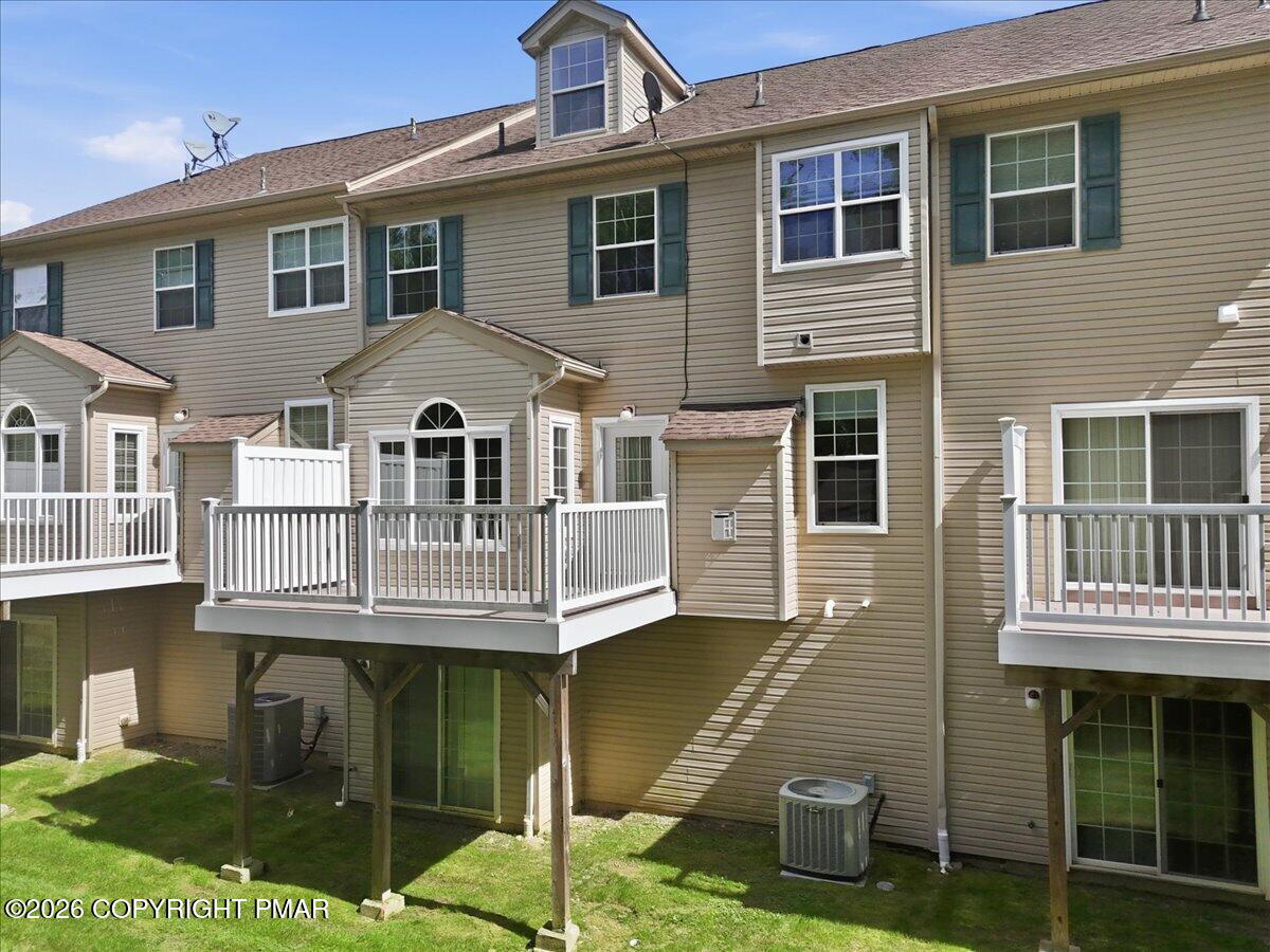 Rear exterior of a tan townhouse with multiple raised, white-railed decks.