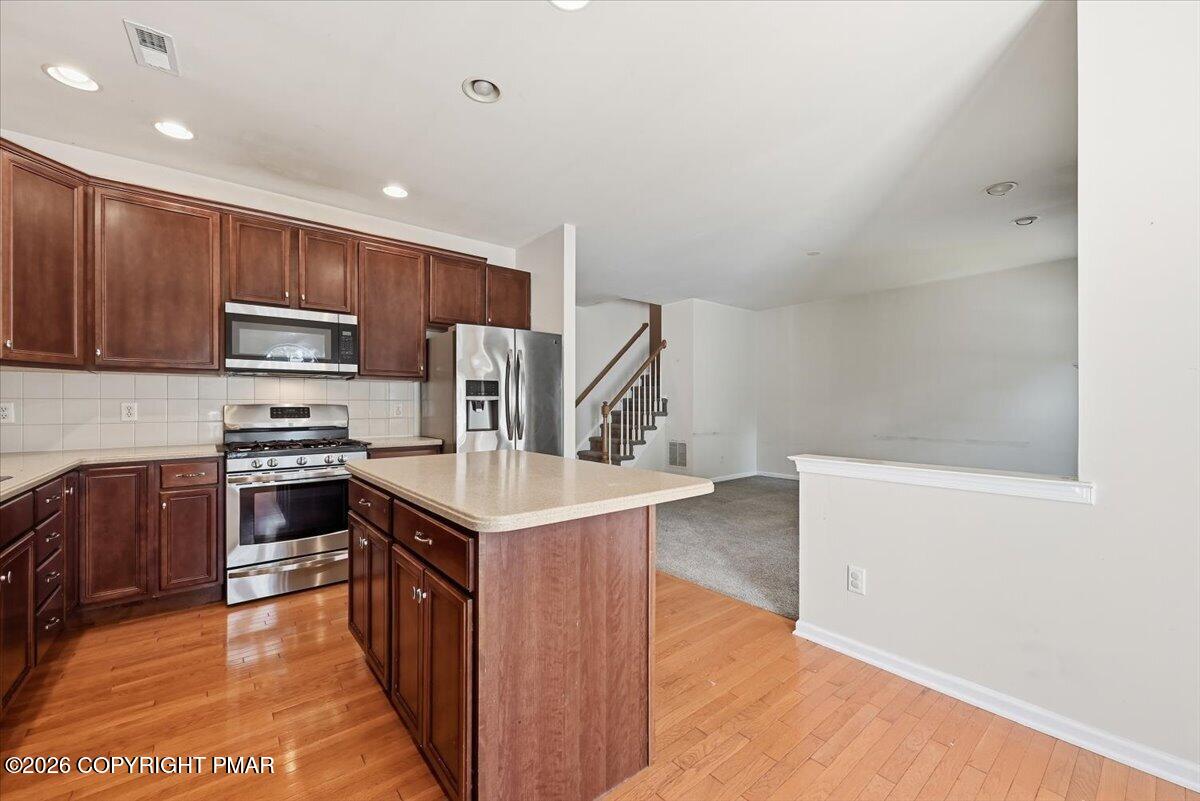 Kitchen with dark wood cabinets, stainless steel appliances, and a large island beside an open living area.