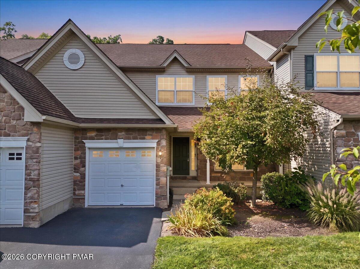 Two-story home with stone accents, attached garage, and landscaped front yard at dusk.