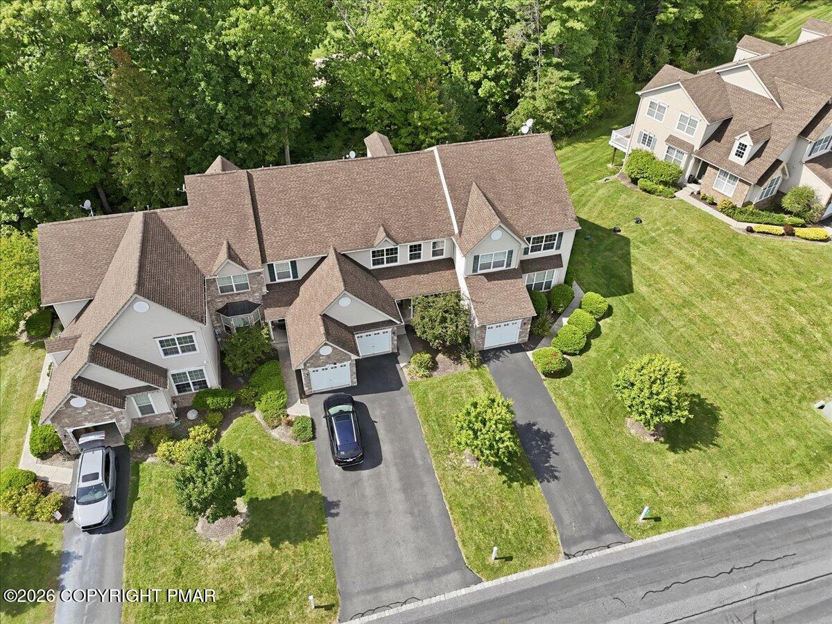 Aerial view of attached homes with driveways, lawns, and mature trees.