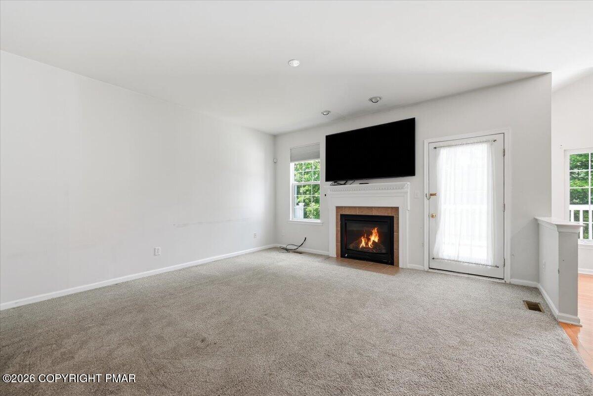 Living room with a carpeted floor, fireplace, mounted television, and glass door with sheer curtains.