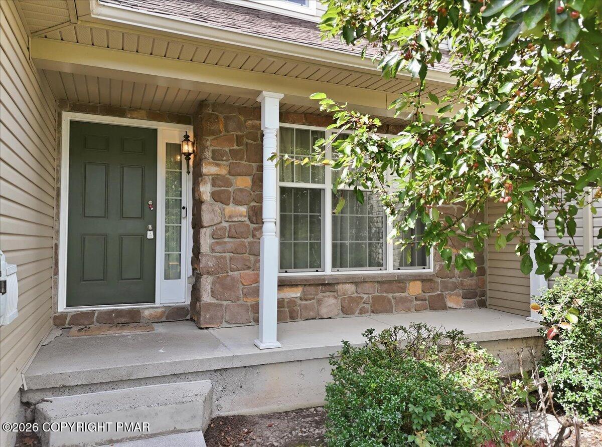 Stone-front home entry with a dark green door, covered porch, and concrete steps.