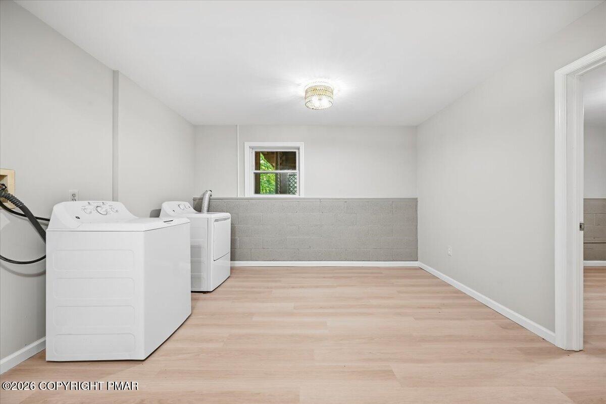 Laundry room with a washer and dryer, pale wood flooring, and a low gray block wall.