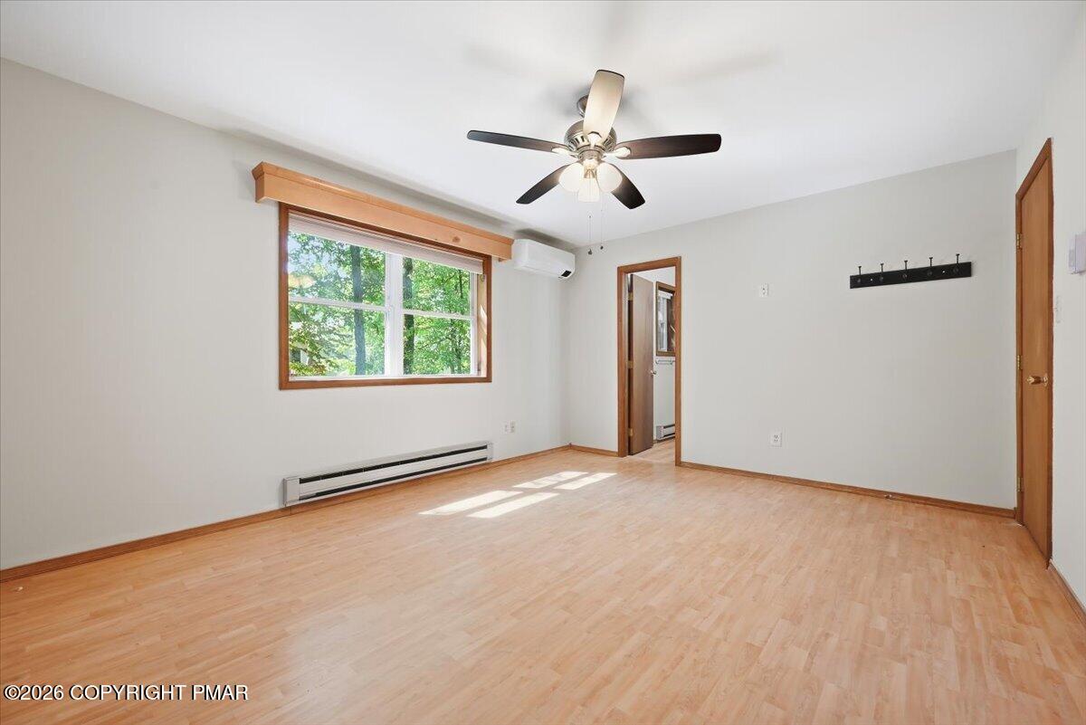 Empty room with wood floors, a tree-facing window, ceiling fan, and wall-mounted mini-split air conditioner.