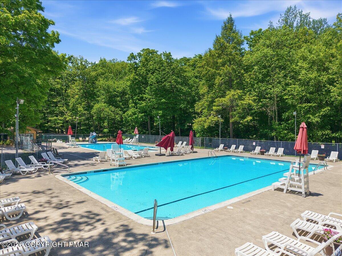 Outdoor swimming pool surrounded by trees, with lounge chairs and red umbrellas on the deck.