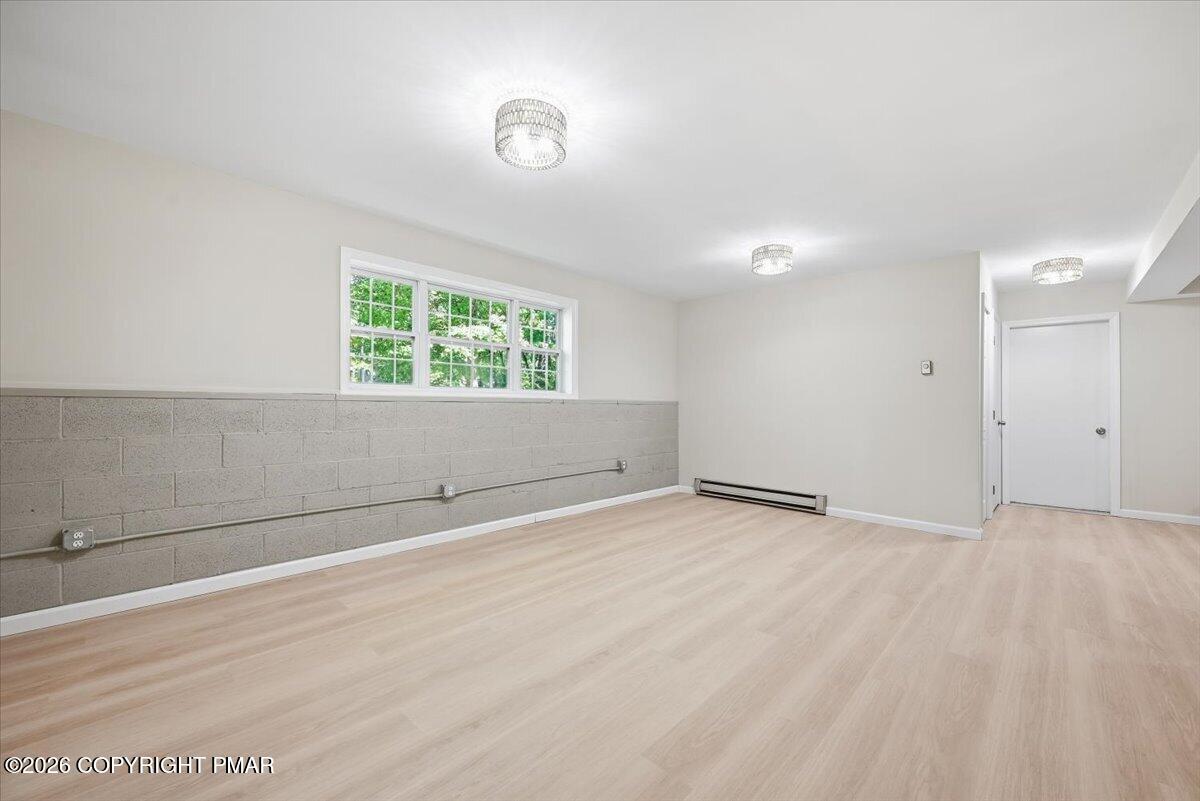 Empty finished basement with pale wood-look flooring, a gray block wall, and wide windows.