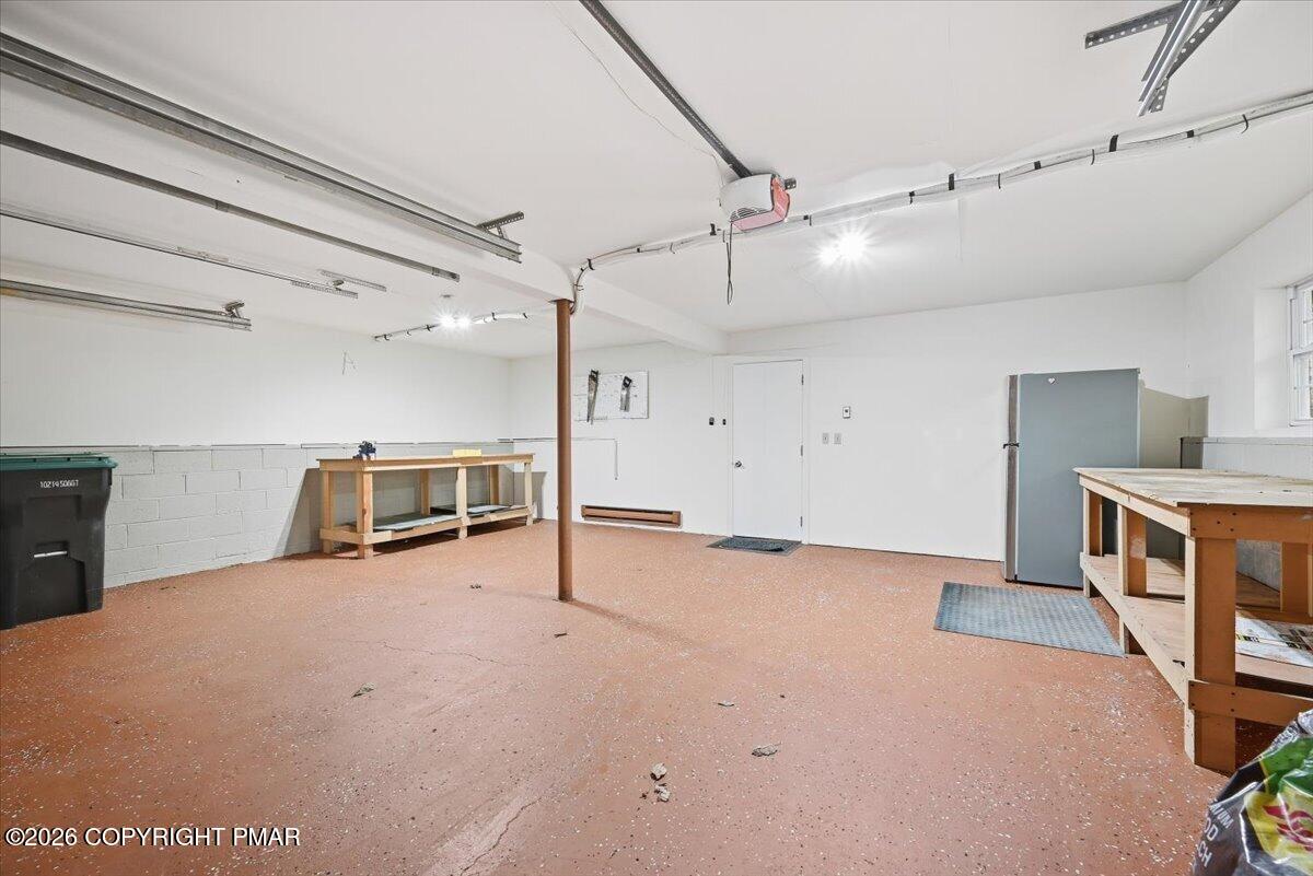 Garage with overhead door tracks, wooden workbenches, and a tall gray storage cabinet.