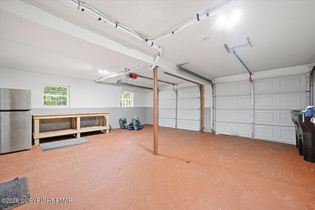 Spacious garage with three overhead doors, a wooden workbench, refrigerator, and reddish speckled floor.