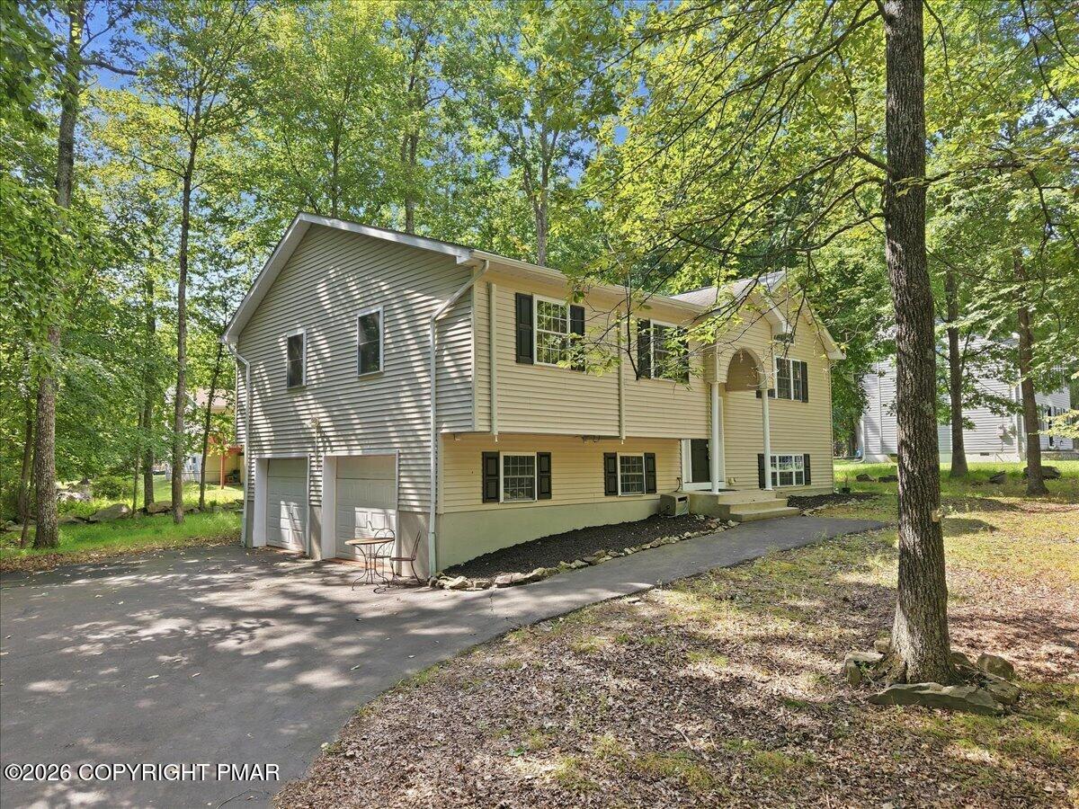 Beige split-level home with an attached two-car garage and curved driveway among mature trees.