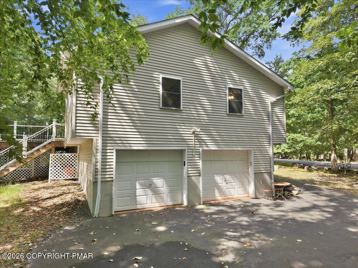 Gray-sided home with two garage doors, a raised deck, and a tree-shaded driveway.
