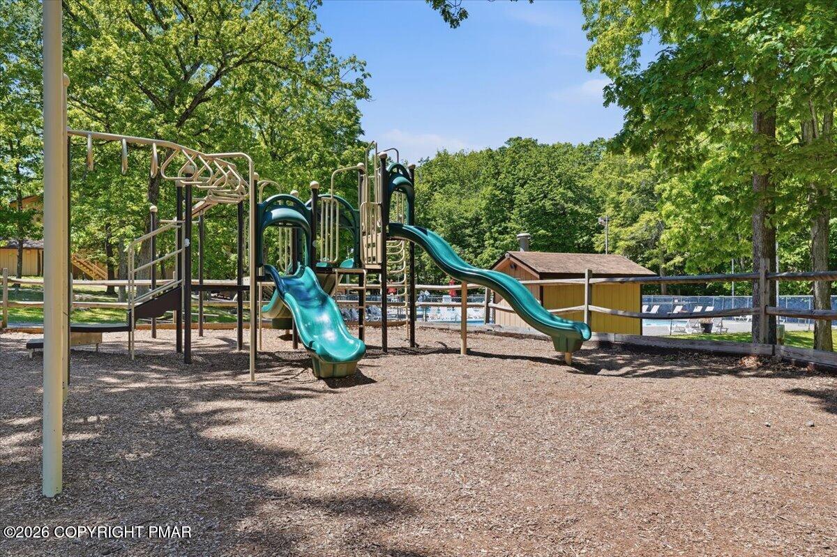 Community playground with teal slides, wooded surroundings, and a pool visible behind it.