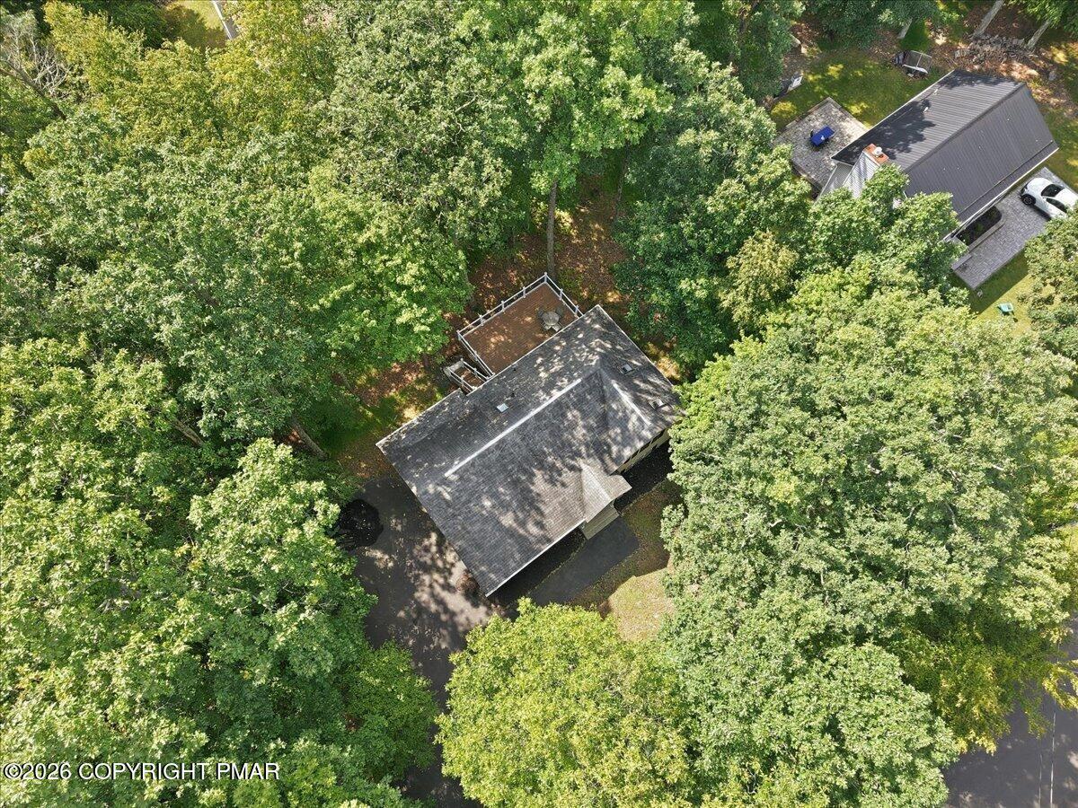Aerial view of a house nestled among dense trees, with a deck and driveway.