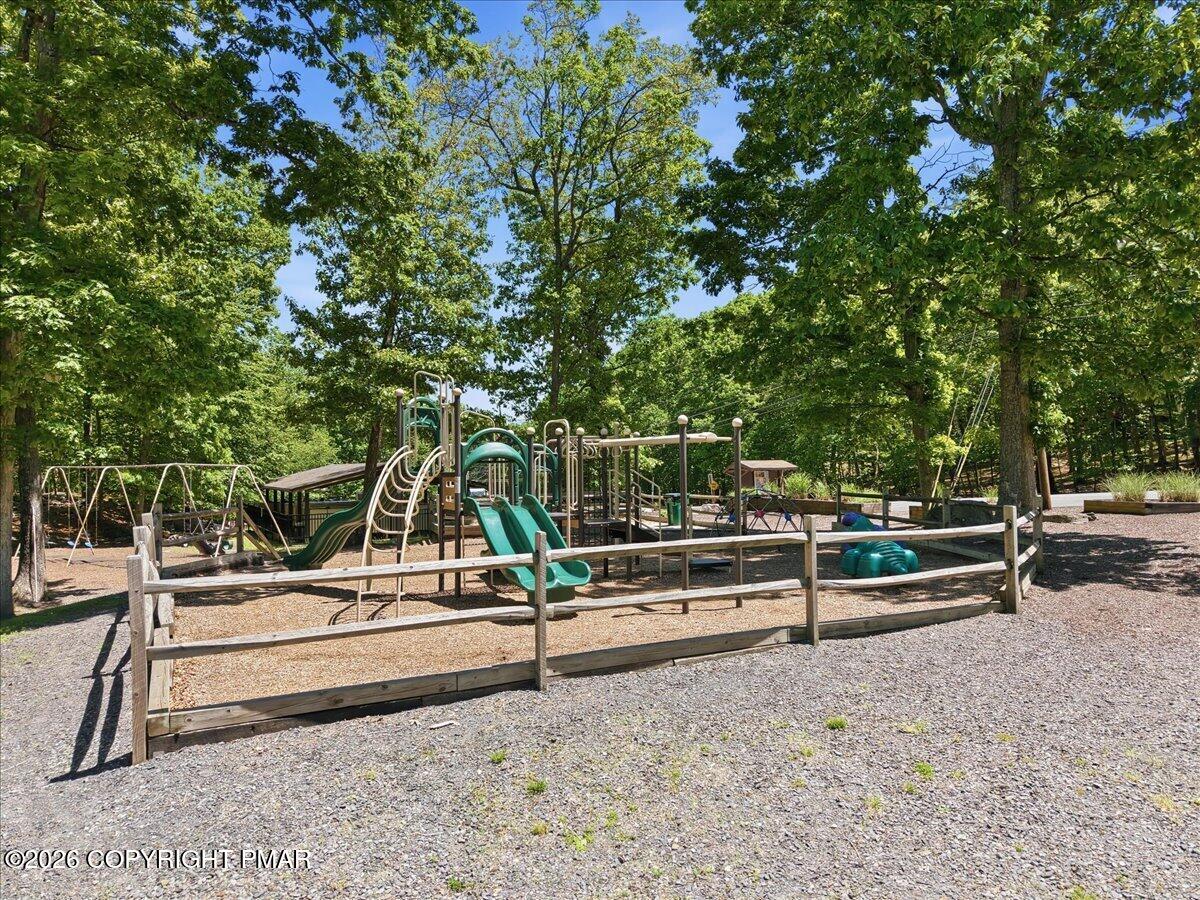 Wooded playground with swings, climbing structures, and slides inside a low wooden fence.