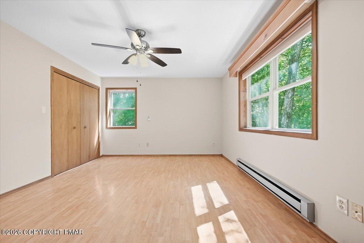 Vacant bedroom with wood flooring, a ceiling fan, and large windows overlooking trees.