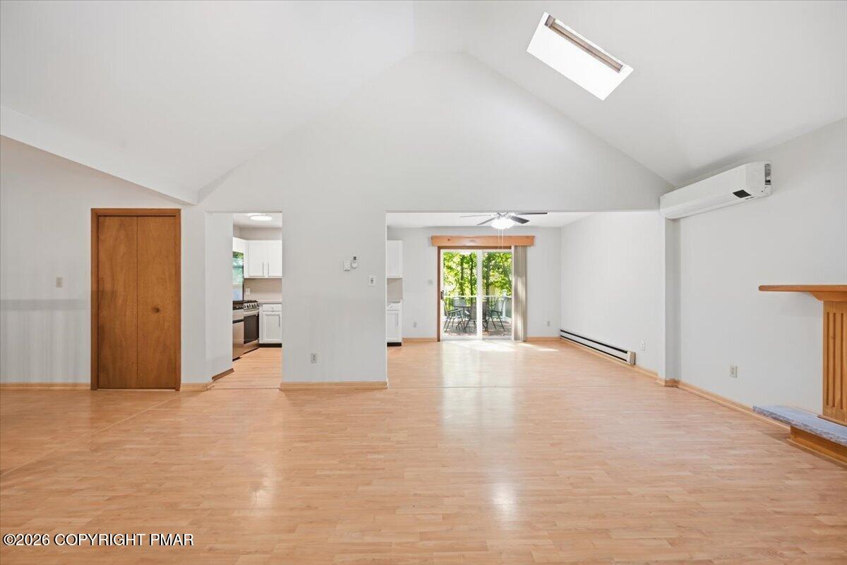 Vacant living room with vaulted ceiling, light wood floors, and sliding doors to a deck.