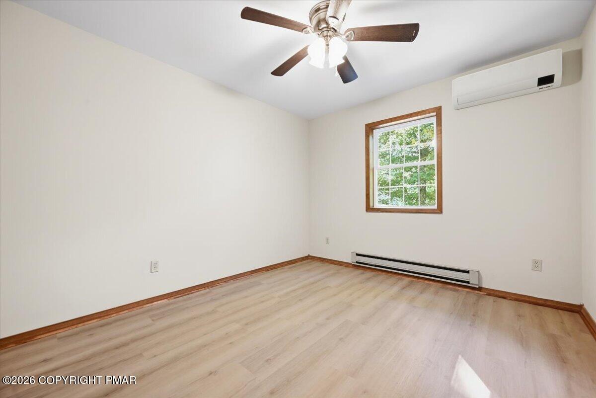 Vacant bedroom with pale wood floors, a ceiling fan, and a wall-mounted mini-split air conditioner.