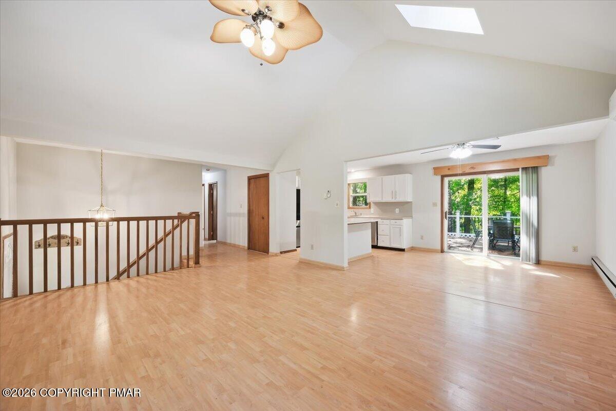 Open living area with light wood floors, a stair railing, and sliding doors to a tree-lined patio.