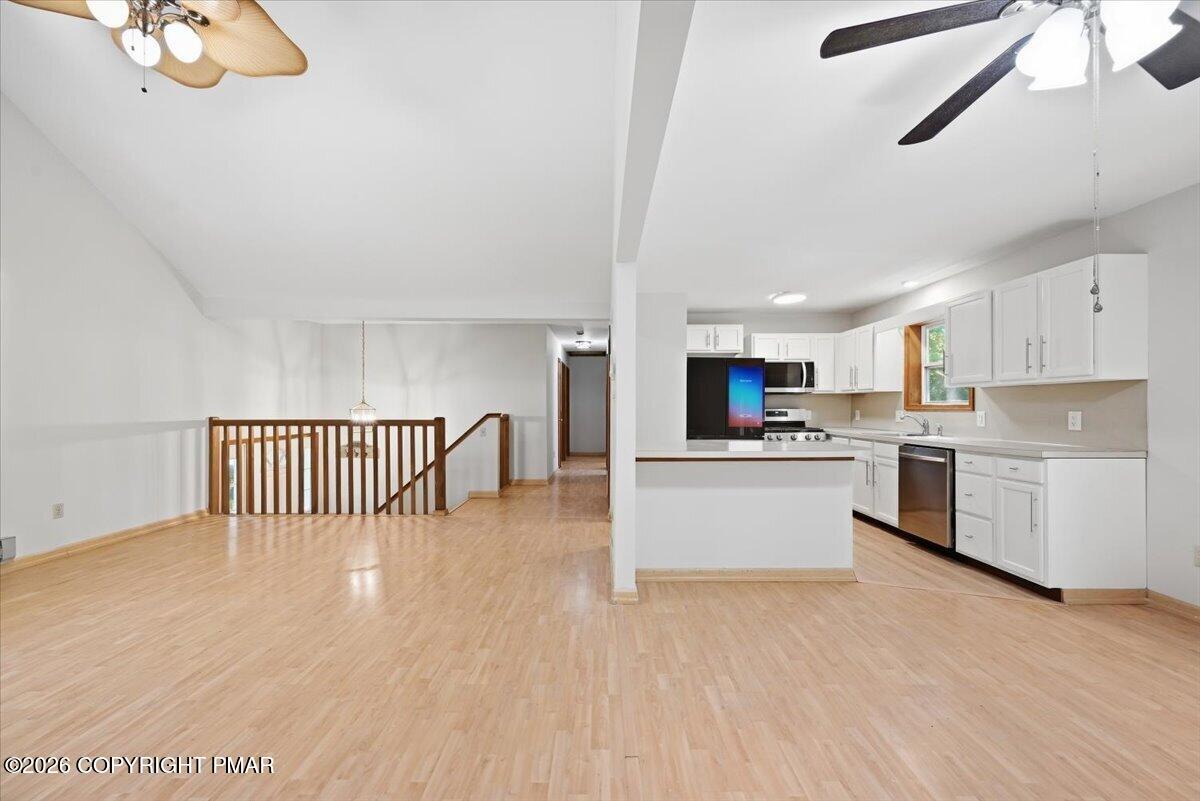 Open kitchen and living area with white cabinets, stainless steel appliances, and light wood flooring.