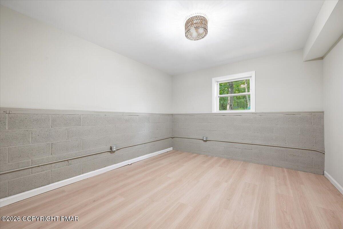 Vacant room with pale wood-look flooring, gray block walls, and a window overlooking trees.
