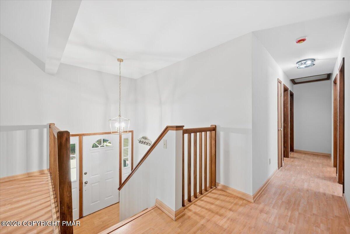 Entryway and upper landing with wood railings, a white front door, and light wood-tone flooring.