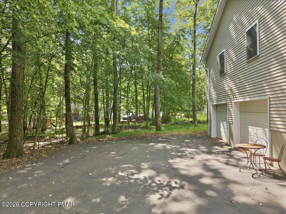 Home’s garage and paved driveway shaded by mature trees, with a small metal patio table and chairs.