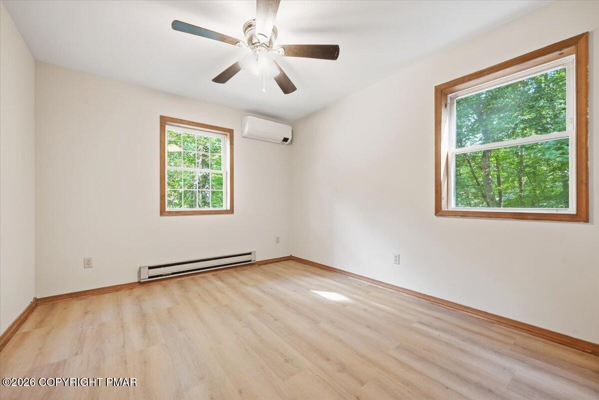 Empty bedroom with light wood floors, two wood-trimmed windows, and a ceiling fan.