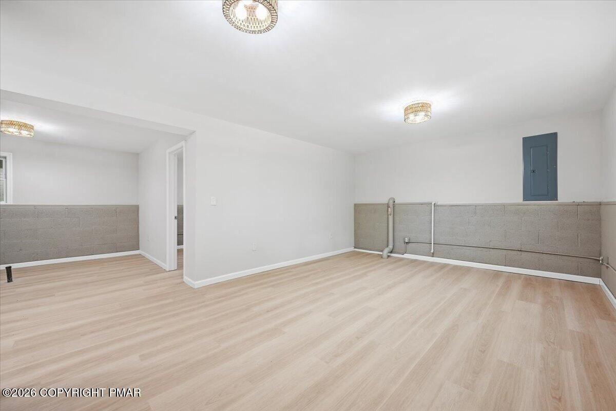 Finished lower-level room with light flooring, gray blockwork, exposed pipes, and ceiling lights.