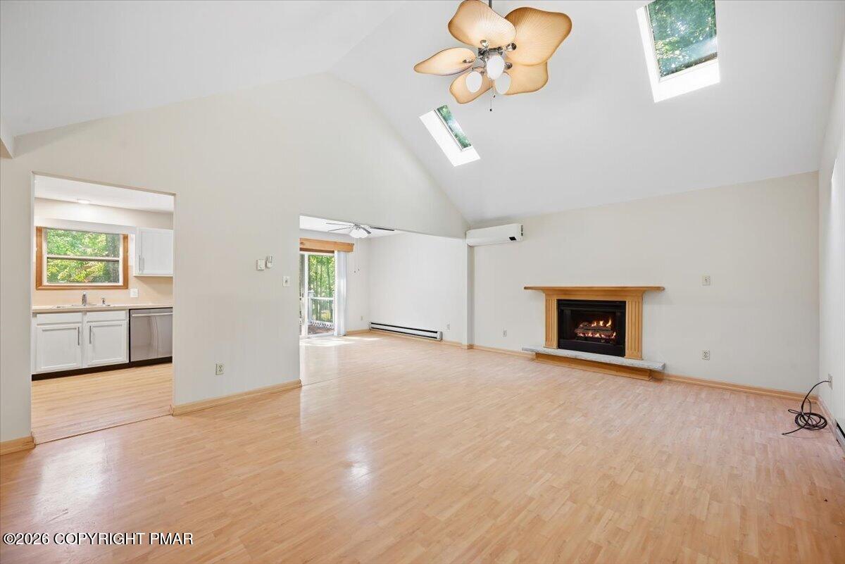 Vacant living room with vaulted skylit ceiling, wood flooring, and a fireplace.